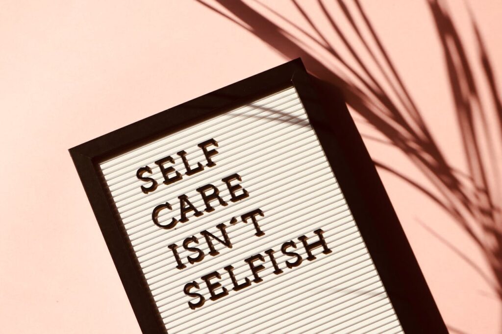 pexels-photo-2821823 Letter board displaying 'Self Care Isn't Selfish' with artistic shadow on pink background.